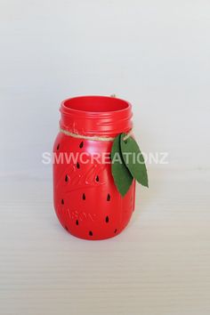 a red mason jar with a green leaf on the top, sitting on a white surface