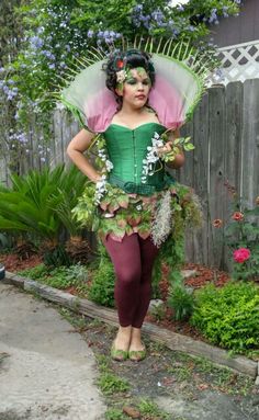 a woman dressed up as a fairy standing in front of a fence