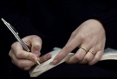 a person holding a pen and writing on a piece of paper with two rings around their fingers