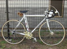 a white and gold bicycle parked next to a fence in front of a metal gate