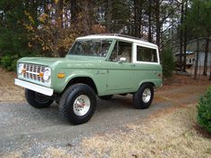 an old ford bronco is parked on the side of the road in front of some trees