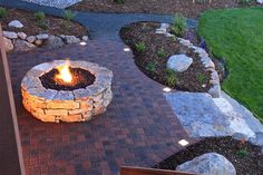 a fire pit sitting on top of a brick patio next to a lush green field