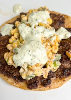 a flatbread topped with meat and vegetables covered in ranch dressing on a white plate