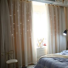 a bed room with a neatly made bed next to a window covered in white curtains