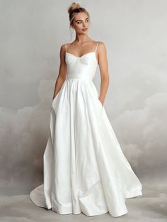 a woman in a white wedding dress standing on a cloud filled background with her hands behind her back