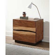 a nightstand with a lamp on top of it next to a rug and a wall