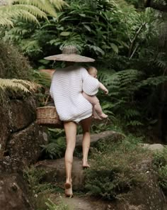 a woman holding a baby in her arms while walking up some steps through the woods