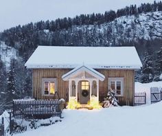 a small house is covered in snow and lit up with christmas lights on the front porch