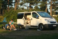 two people sitting at a table in front of a camper van with the door open