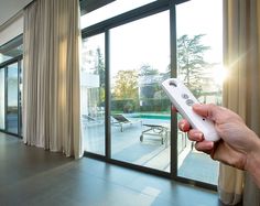 a hand holding a remote control in front of a sliding glass door that leads to a swimming pool