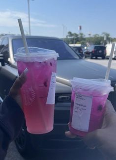 two people holding up drinks in front of a car