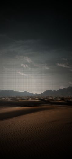 an empty desert with mountains in the distance and dark clouds over it at night time