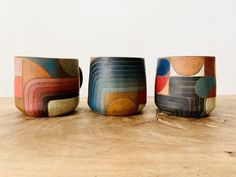 three colorful cups sitting on top of a wooden table next to each other and one is empty