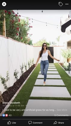 a woman in white shirt and jeans walking down a long walkway with grass on both sides