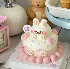 a white cake with pink frosting and bunny ears on top, sitting next to a teddy bear