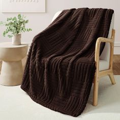 a brown blanket sitting on top of a white chair next to a potted plant