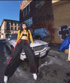 a woman standing on top of a car in front of a graffiti covered wall and building