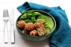 a bowl filled with meatballs and vegetables next to a fork, knife and napkin