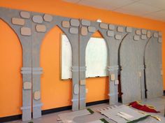 an orange wall with arches and windows in the middle, surrounded by cut out pieces of paper