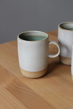 two coffee mugs sitting on top of a wooden table next to each other,