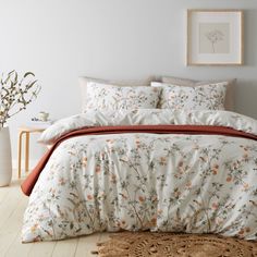 a bed with white and orange comforters in a room next to a plant on the floor