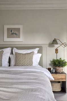 a bed with white linens and pillows in a bedroom next to a painting on the wall