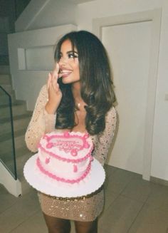 a woman holding a pink and white cake in front of her face while standing next to stairs