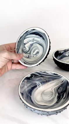 two black and white marbled bowls being held by a person's hand on a white surface