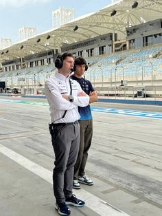 two men standing in front of an empty race track with headphones on their ears