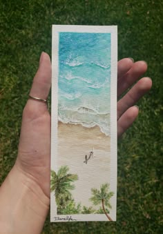 a person holding up a card with an image of two birds on the beach and palm trees