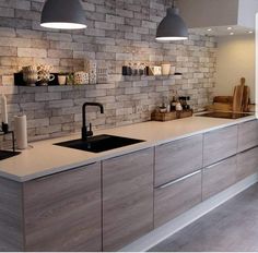 a kitchen with grey cabinets and white counter tops next to a brick wall that has hanging lights above it