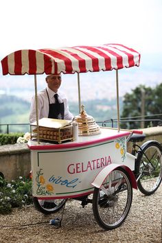 a man is selling food from a cart on the side of a road with a red and white striped awning