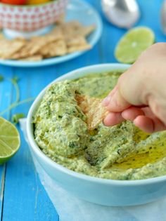 a hand dipping a tortilla chip into a bowl of guacamole