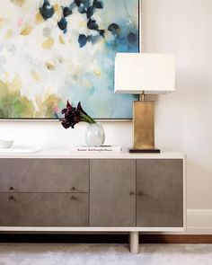 a vase with flowers sitting on top of a dresser next to a painting and lamp