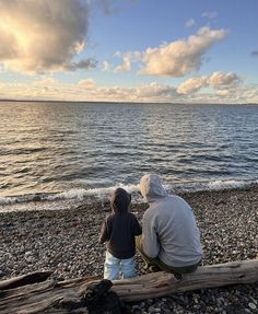 an older man and young boy sitting on a log looking out at the ocean