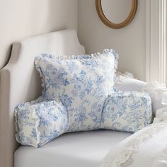 a white chair with blue and white pillows on it next to a round mirror in a room