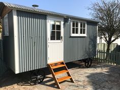 a tiny house with a ladder next to it and a tree in the back ground