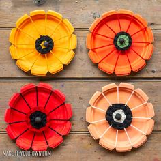 four different colored plates sitting on top of a wooden table next to an orange, yellow, and red flower