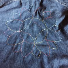 the back of a jean jacket with stitching on it's side and an embroidered flower