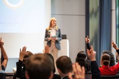 a woman standing in front of a crowd holding her hands up to the sky while giving a speech