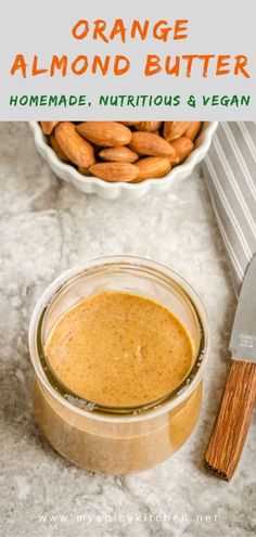 an orange almond butter in a glass jar next to a bowl of peanuts and a knife