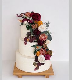 a three tiered wedding cake with flowers on the top and bottom, sitting on a wooden stand