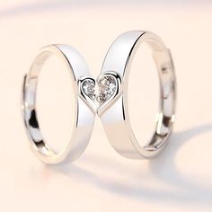 two white gold wedding rings with heart shaped diamond in the middle, on a light background