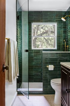 a bathroom with green tile walls and a white toilet sitting next to a walk in shower