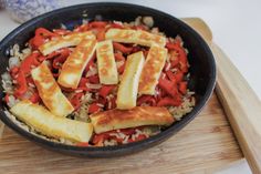 a pan filled with rice and vegetables on top of a wooden cutting board