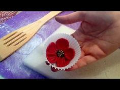 a person is holding a paper cupcake with a red flower on it and a wooden spatula in the background