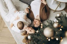 two women and a baby laying on the floor next to a christmas tree with ornaments