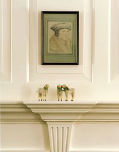 two sheep figurines sitting on top of a mantle in front of a painting