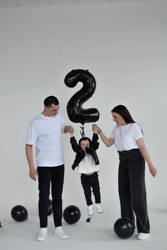 three people standing in front of a balloon shaped like the number two, with one person holding