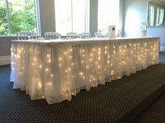 a long table with white chairs and lights on it is set up for an event